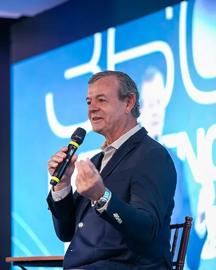 Palestrante ao microfone no palco da 1ª edição, diante do painel azul